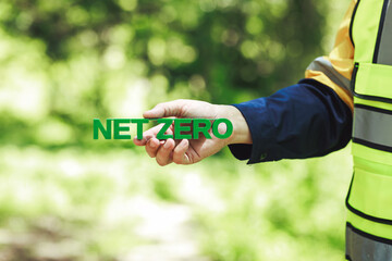 Naklejka premium Construction worker in a high visibility vest holds a green net zero sign outdoors, commitment to sustainability and lower carbon emissions.
