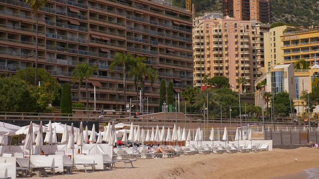 Outdoor beach club terrace with rows of white furniture beneath Monaco high rise buildings near the Mediterranean waterfront 4K. 7 May 2019