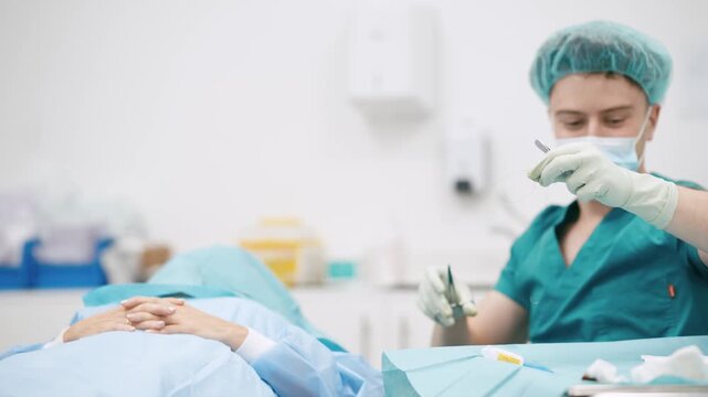 Male surgeon in sterile uniform, mask, and gloves suturing a patient during a medical procedure in a bright, modern hospital operating room