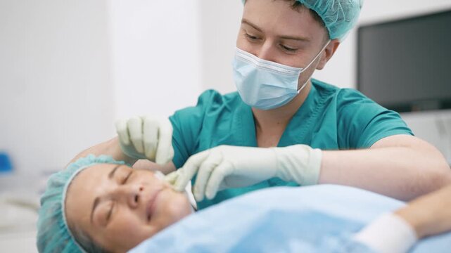 Male surgeon in scrubs performing a cosmetic procedure on a woman's face. Professional doctor doing an aesthetic treatment in a clinic