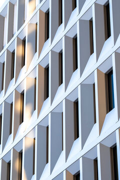 White modern facade with deep windows and angular geometric frames creating a repeating pattern of light and shadow across contemporary urban architecture