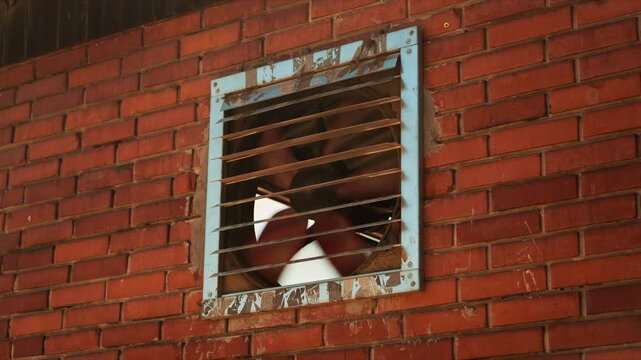 Industrial farm ventilation fan behind metal grid on red brick wall, 4K
