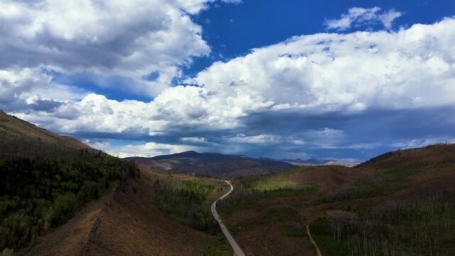 Aerial view of a winding road through a mountain valley with dramatic clouds and patches of sunlight over the landscape in Granby, Colorado, United States.