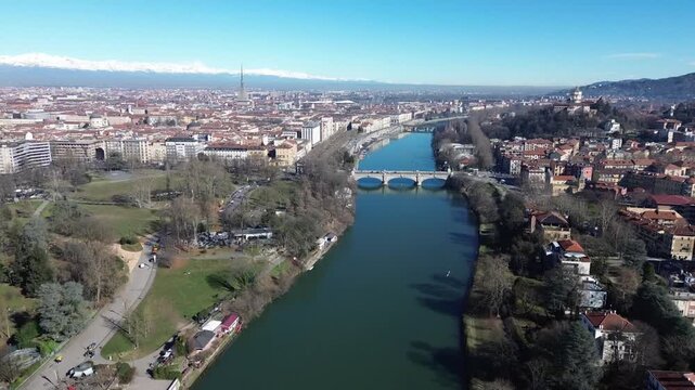 Aerial drone view capturing Po River, Umberto I bridge, Valentino Park and landmark Mole Antonelliana dome with snowy Italian Alps in background, Turin, Piedmont, Italy