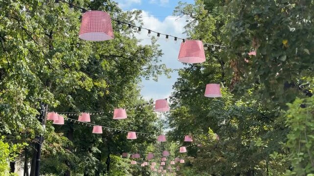 Outdoor string lights with pink lampshades hanging in a lush green park, creating a festive atmosphere