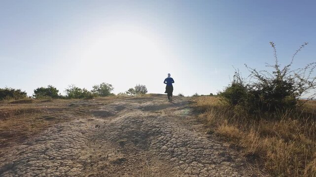 Trail runner moving across dry open terrain determined pace drone tracking