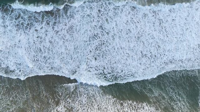 Aerial view of ocean waves crashing against the sandy coastline in Pacitan, East Java, Indonesia.