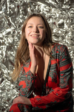 Young beautiful woman in a red patterned dress posing against a shiny silver foil background