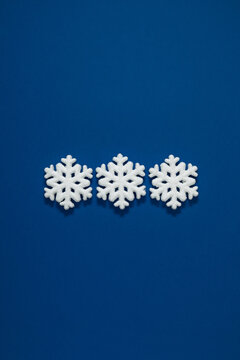 Minimalist Christmas flat lay with three white glitter snowflakes lined up in center on a classic blue background with large empty copy space for winter holiday greeting text design