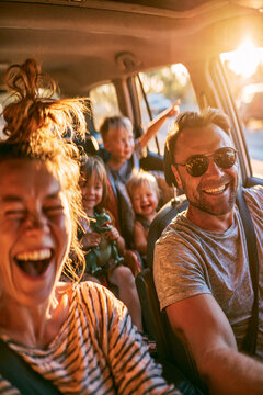 A wide angle shot captures a family of five on a road trip inside a moving SUV, having a great time, laughing.