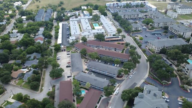 Terraced apartment buildings line Mahncke Park in Bexar County edge near Broadway. Brown shingled residential roofs frame sunny courtyard pools, parking bays, lots, San Antonio, Texas