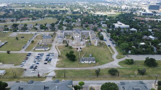 Limestone military quadrangle anchors Mahncke Park in Bexar County edge near Broadway. Historic masonry barracks border organized vehicle lots, wide green lawns, paved roads, San Antonio, Texas