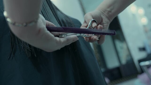 The hairdresser's hands with scissors trim the ends of the hair