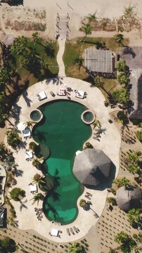 Aerial view of the swimming pool at Cerritos Beach resort with palm trees and thatched palapas in Todos Santos, Baja California, Mexico.
