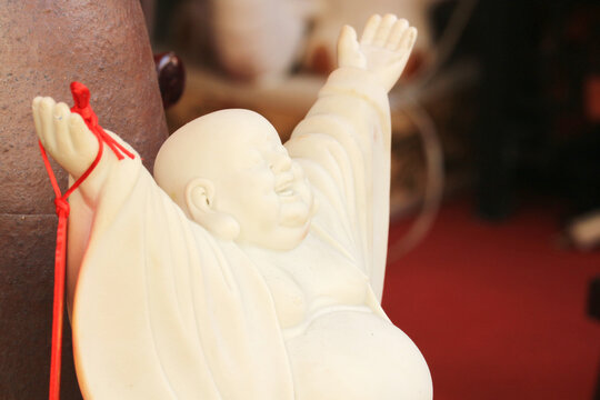 Close-up view of a white ceramic Laughing Buddha statue with raised arms on a blurred background.