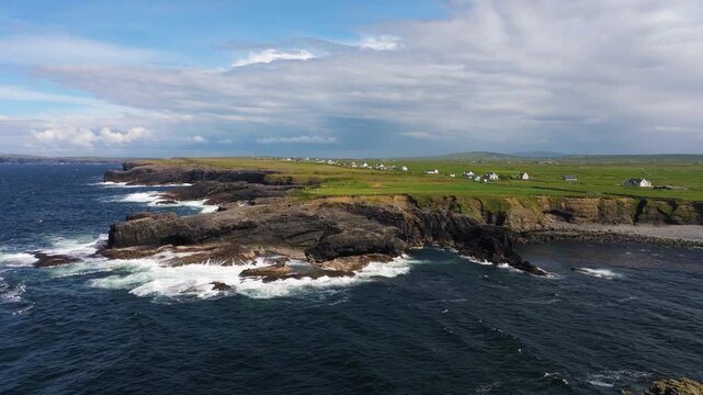 Aerial view of rugged coastline with crashing waves and green fields along the atlantic ocean in county clare ireland.