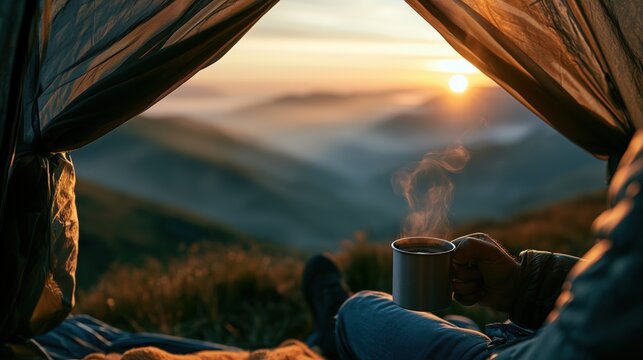 A traveler sits outside a camping tent with a metal mug of hot coffee as sunrise illuminates misty mountains, creating a peaceful and cozy outdoor escape.