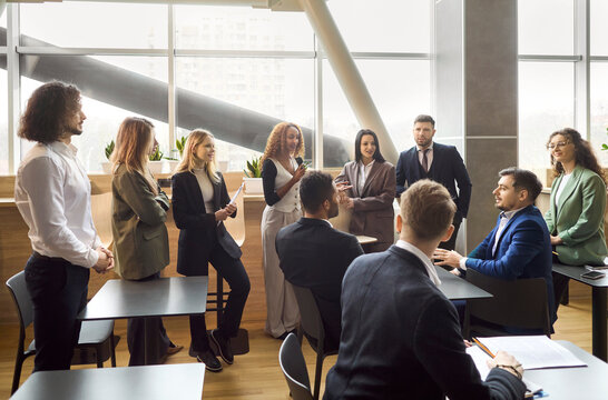 Team training meeting with coach in office discussion. A diverse group of professionals stands together, sharing ideas during a corporate briefing and aligning goals. Team unity and growth rise.