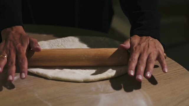 A woman rolls out dough with wooden rolling pin on a dinning table