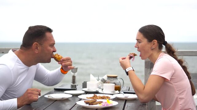High quality video of a happy couple enjoying a seafood lunch at an outdoor sea cafe during a cycling trip.