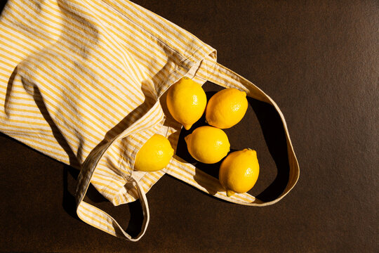 Citrons jaunes sortant d'un sac &agrave; rayures jaunes et blanches pos&eacute; sur un fond brun fonc&eacute;, vue du dessus, image vive et contrast&eacute;e