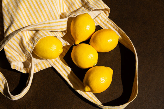 Citrons jaunes en gros plan sortant d'un sac &agrave; rayures jaunes et blanches sur un fond brun fonc&eacute;, retour de march&eacute;, vue du dessus, image lumineuse et contrast&eacute;e