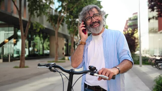 Senior man talking on mobile phone while leaning on bicycle after cycling in urban city