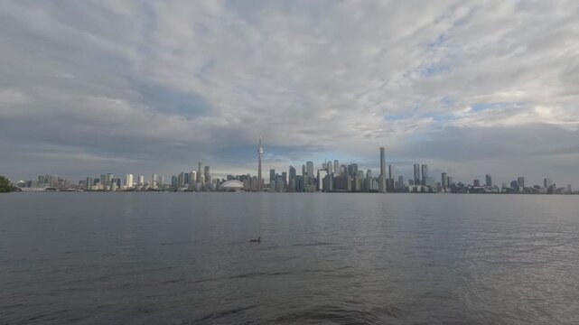 Wide timelapse of Toronto skyline and calm Lake Ontario waterfront from Toronto Islands, with drifting clouds and a ferry approaching at the end.