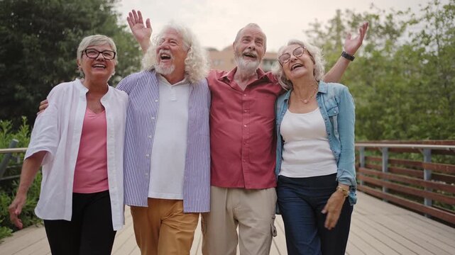 Happy senior friends walking and laughing together in city park enjoying active retirement lifestyle