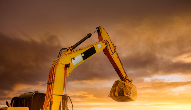 Backhoe excavator digging soil at construction site at sunset. Hydraulic arm and bucket lifting dirt for trenching, earthmoving and infrastructure development. site preparation and civil engineering.