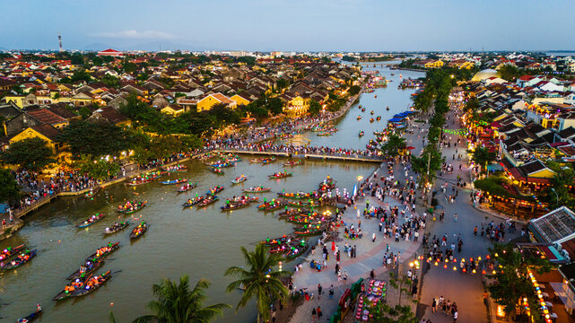 Aerial view of the historic Hoi An Ancient Town with traditional wooden boats on the Thu Bon River, illuminated lanterns, and crowds of people in Hoi An, Da Nang, Vietnam.