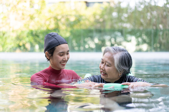 A healthcare caregiver assists an older woman during a relaxing hydrotherapy exercise in a swimming pool. The image highlights rehabilitation, trust, and active senior living