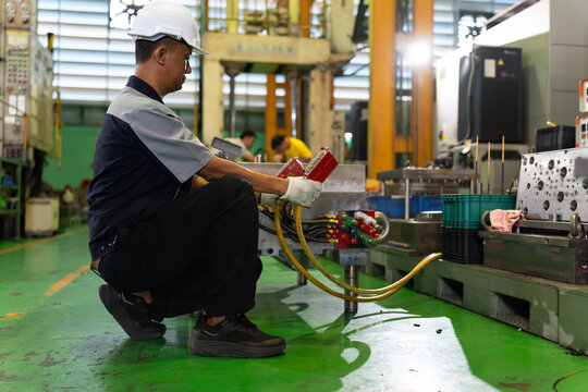 A factory technician adjusts industrial machine connections while working beside manufacturing equipment inside a factory. Concept of equipment setup, maintenance, workplace safety