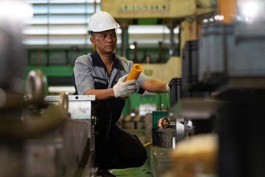 A factory worker installs an industrial machine component beside heavy manufacturing equipment inside a production facility. Concept of precision work, industrial maintenance, and workplace safety