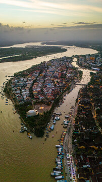 Aerial view of Hoi An ancient town, featuring traditional rooftops, the Thu Bon River, numerous small boats, and bridges at dusk in Hoi An, Da Nang, Vietnam.