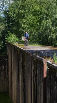 Captivating vertical footage of a male cyclist riding a bicycle along a massive abandoned concrete lock of the historic Mazury Canal in the Kaliningrad region.