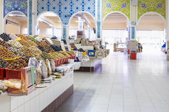 Dried fruits and nuts displayed in heaps at an indoor bazaar in Bukhara, Uzbekistan. Ornamental arches with colorful tile mosaics frame the spacious market hall, ideal for travel and cultural content.