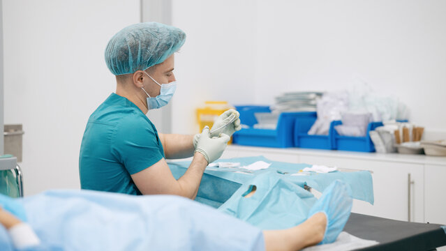 Surgeon wearing scrubs, cap, and mask preparing medical instruments on a sterile table for a medical procedure