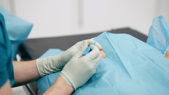 Doctor's gloved hands holding a scalpel, making an incision on a patient covered by sterile drapes during surgery