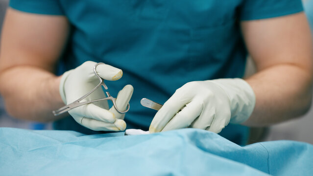 Surgeon wearing sterile gloves performing a medical procedure with surgical tools on a patient covered by a surgical drape