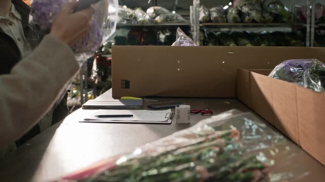 Young adult Caucasian female workers packing fresh flowers into boxes and scanning barcodes in wholesale warehouse, low angle shot. Clip is ideal for logistics and supply chain marketing