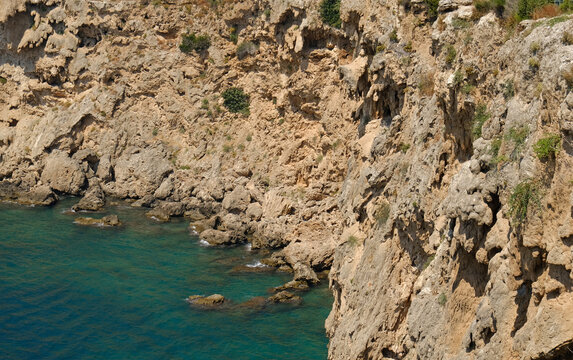 Rocky Mediterranean sea cliff with turquoise water, a rugged coastal landscape. For travel, tourism, nature, and environmental advertising.