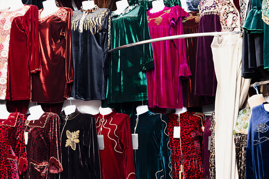 Velvet dresses with gold embroidery displayed on mannequins at an oriental bazaar in Bukhara, Uzbekistan. Colorful traditional garments in rich jewel tones fill the frame, ideal for travel, culture.