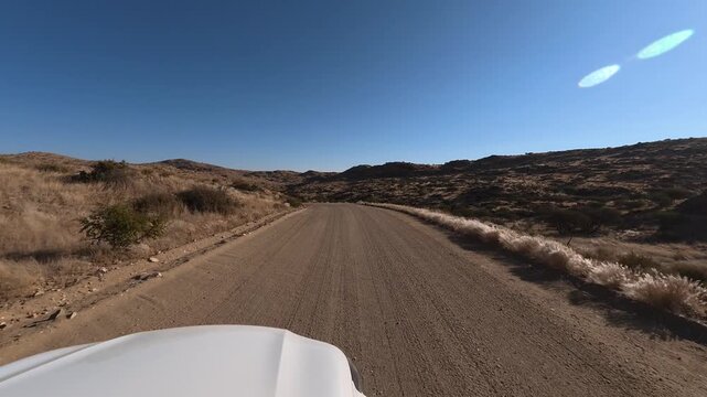 A lone white car drives along a dusty dirt road in Namibia, Africa.