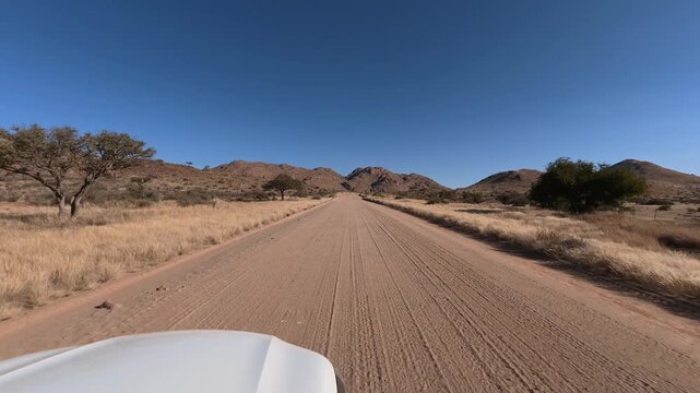 A lone white car drives along a dusty dirt road in Namibia, Africa.