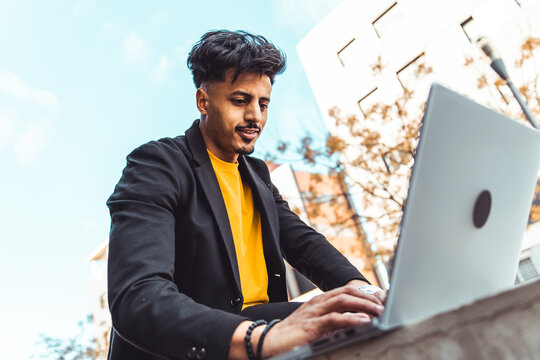 Young Moroccan man entrepreneur managing his online freelance business, typing on a laptop computer in an urban outdoor setting