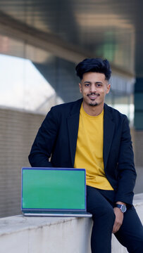 Moroccan businessman smiling, sitting outdoors with a modern laptop showing a green screen for digital content placement