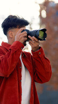 Moroccan man holding a DSLR camera, focusing to take a view outdoors. He is wearing a red corduroy shirt