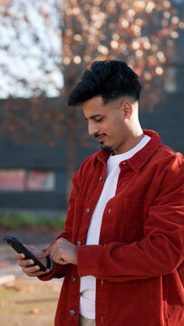 Young Moroccan man engrossed in his mobile phone, connecting and communicating in an outdoor setting during autumn