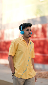 Moroccan man enjoying music with blue headphones, walking in an urban setting. Lifestyle portrait depicting youth and technology